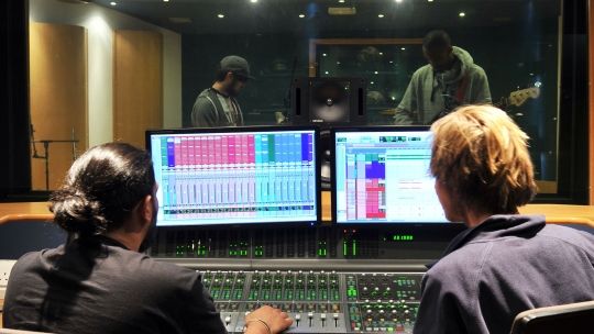 two men looking at two screens in a music studio 
